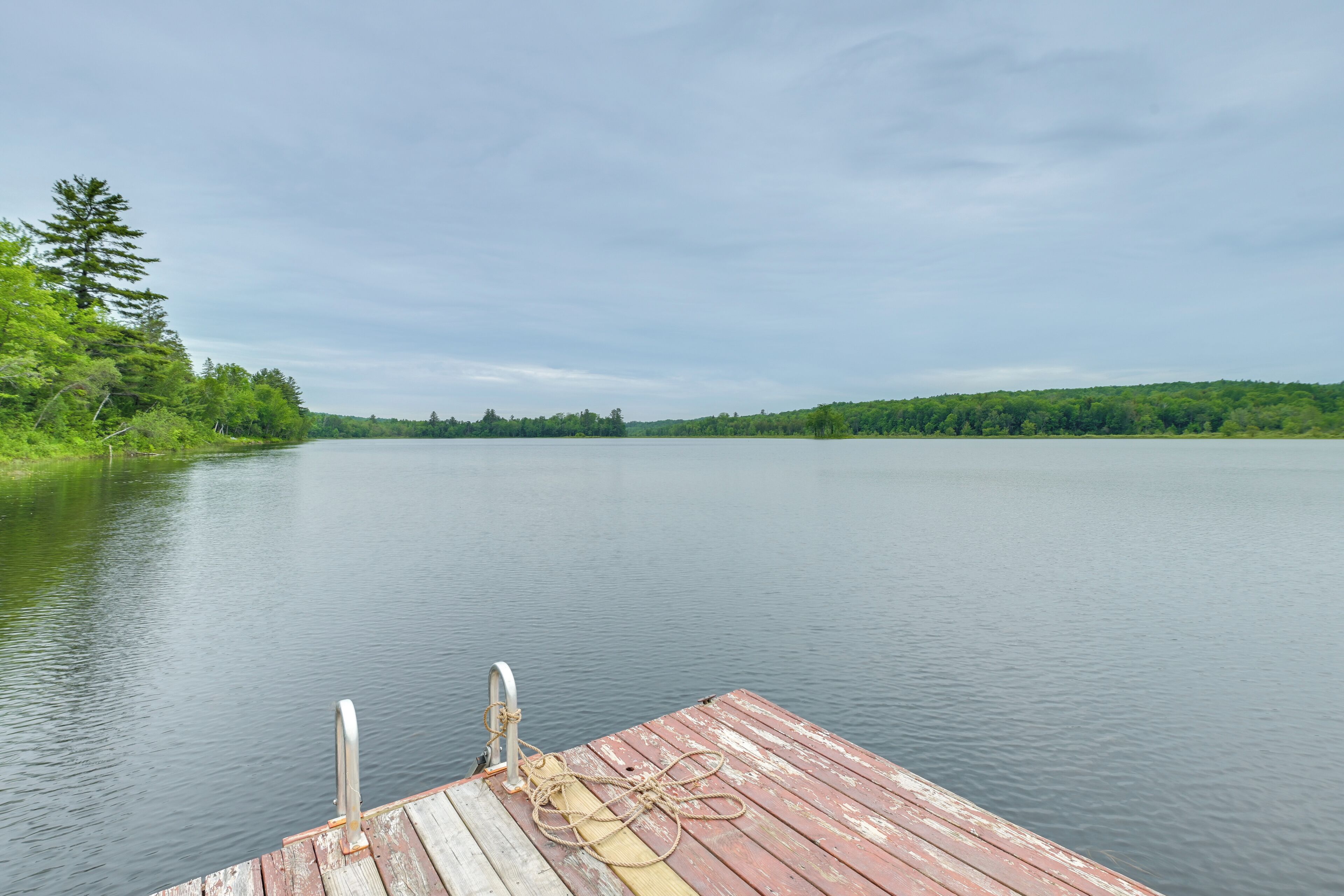 A wooden dock extending into calm water with a forested shoreline in the background.