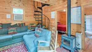 L’intérieur d’un chalet accueillant, avec un canapé bleu, une chaise en bois, un escalier en colimaçon et un poêle à bois.