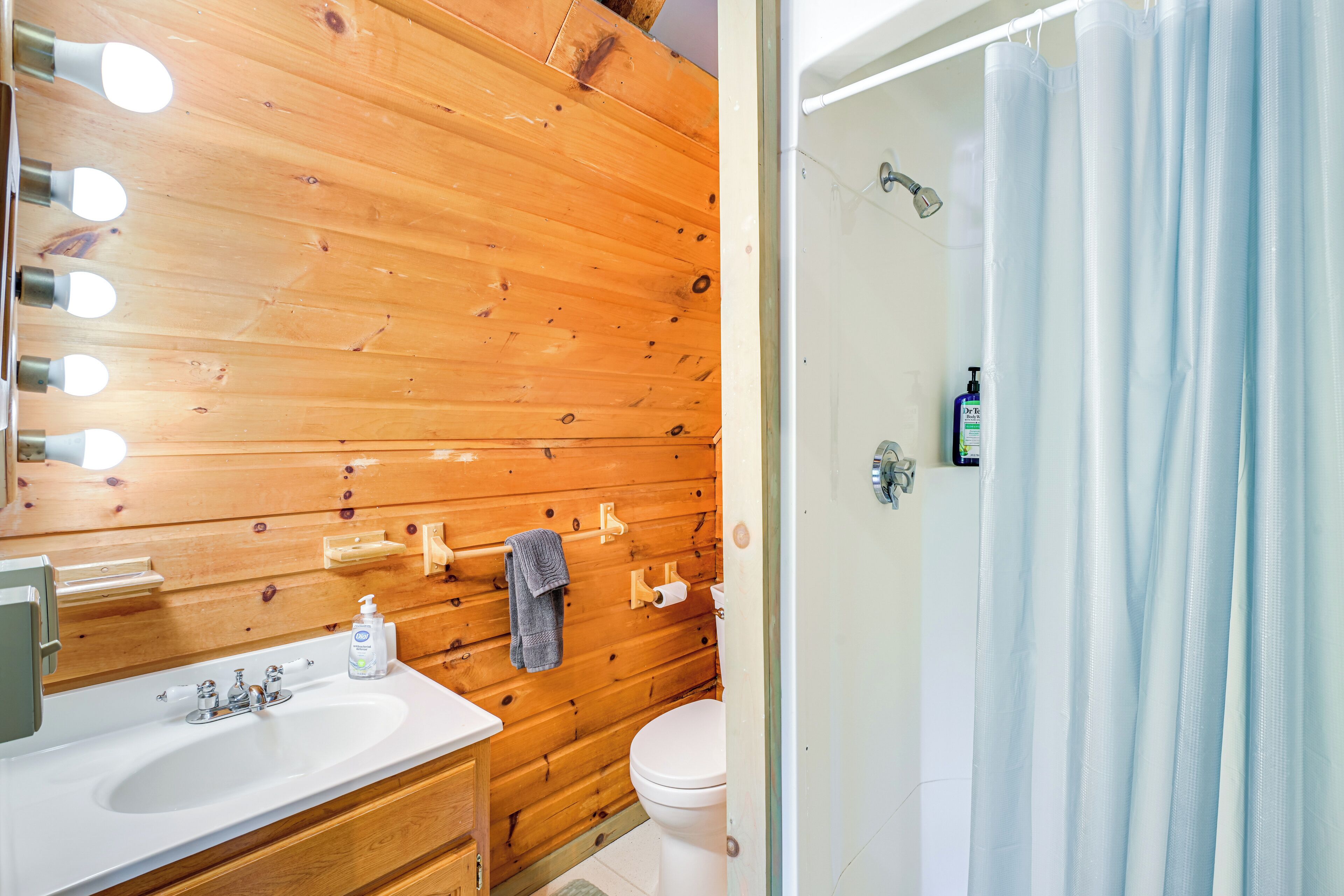 Une salle de bain avec un meuble-lavabo en bois, un évier, un miroir avec éclairage intégré, une serviette suspendue et un rideau de douche.