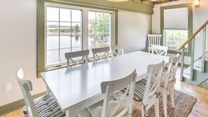 A dining area with a white table and chairs, large windows with a view of a lake, and a wooden ceiling. - Historic Winter Harbor Cottage w/ Waterfront Views (Winter Harbor)