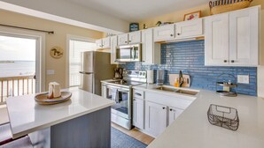 A modern kitchen with white cabinets, a blue-tiled backsplash, stainless steel appliances, and a view to the outside. - Gorgeous Onekama Condo w/ Pool & Lake Access! (Onekama)
