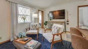 Een moderne woonkamer met een televisie, comfortabele zithoek, een eethoek en een groot raam met gordijnen.