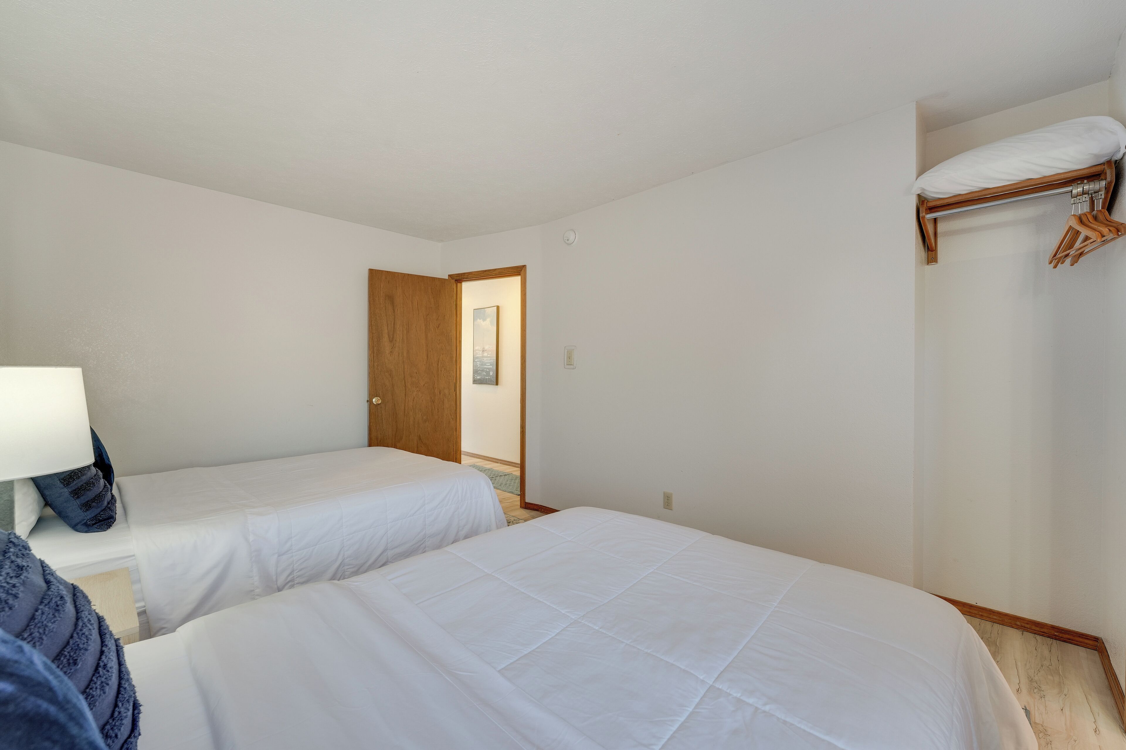 A room with two single beds, a wooden door, a coat rack, and a lamp.