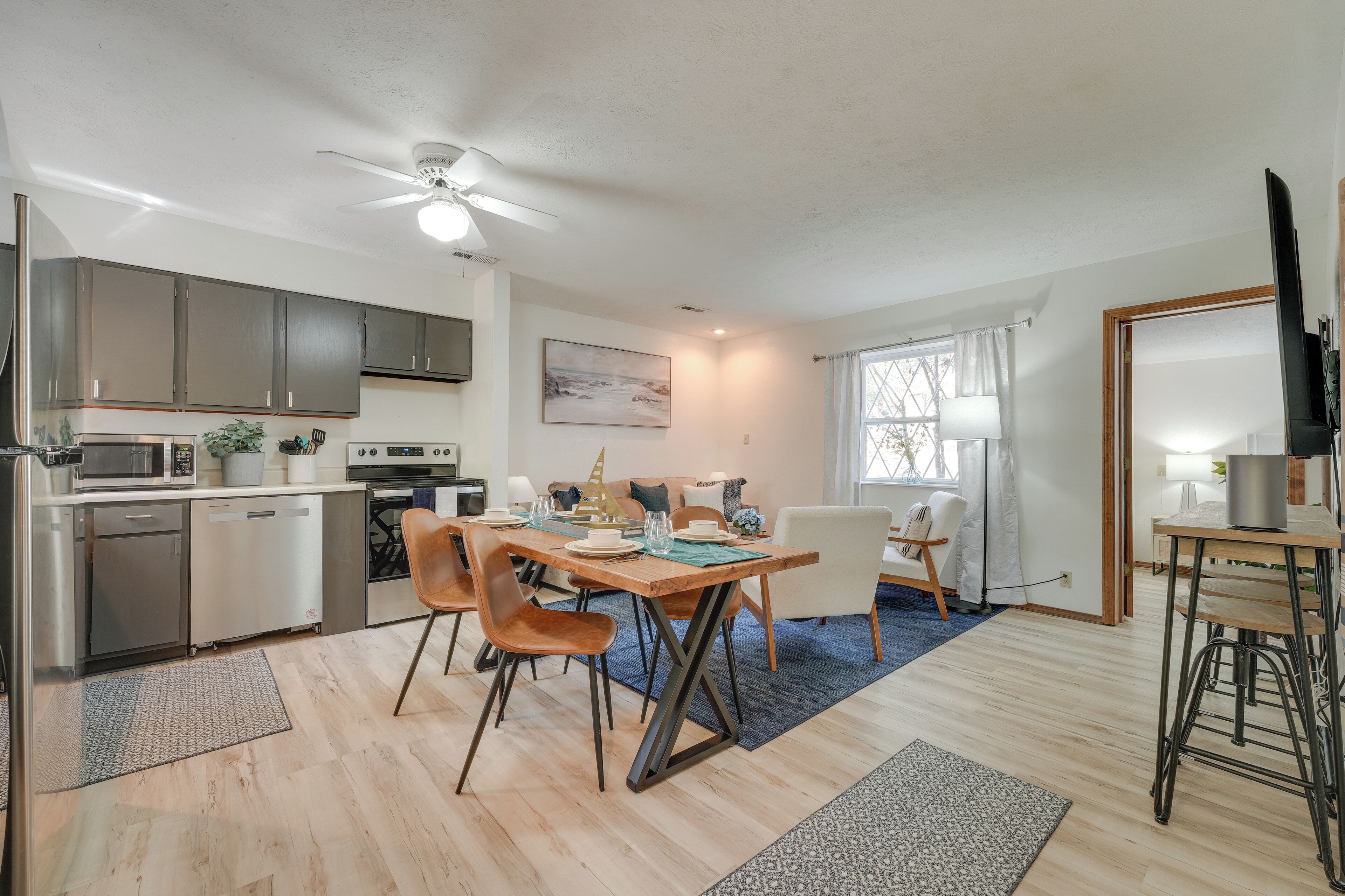 A modern kitchen with stainless steel appliances, a dining area with a wooden table and chairs, and a ceiling fan.
