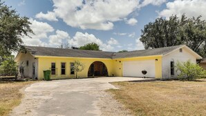 Uma casa amarela com garagem, entrada por automóvel e um pequeno jardim.