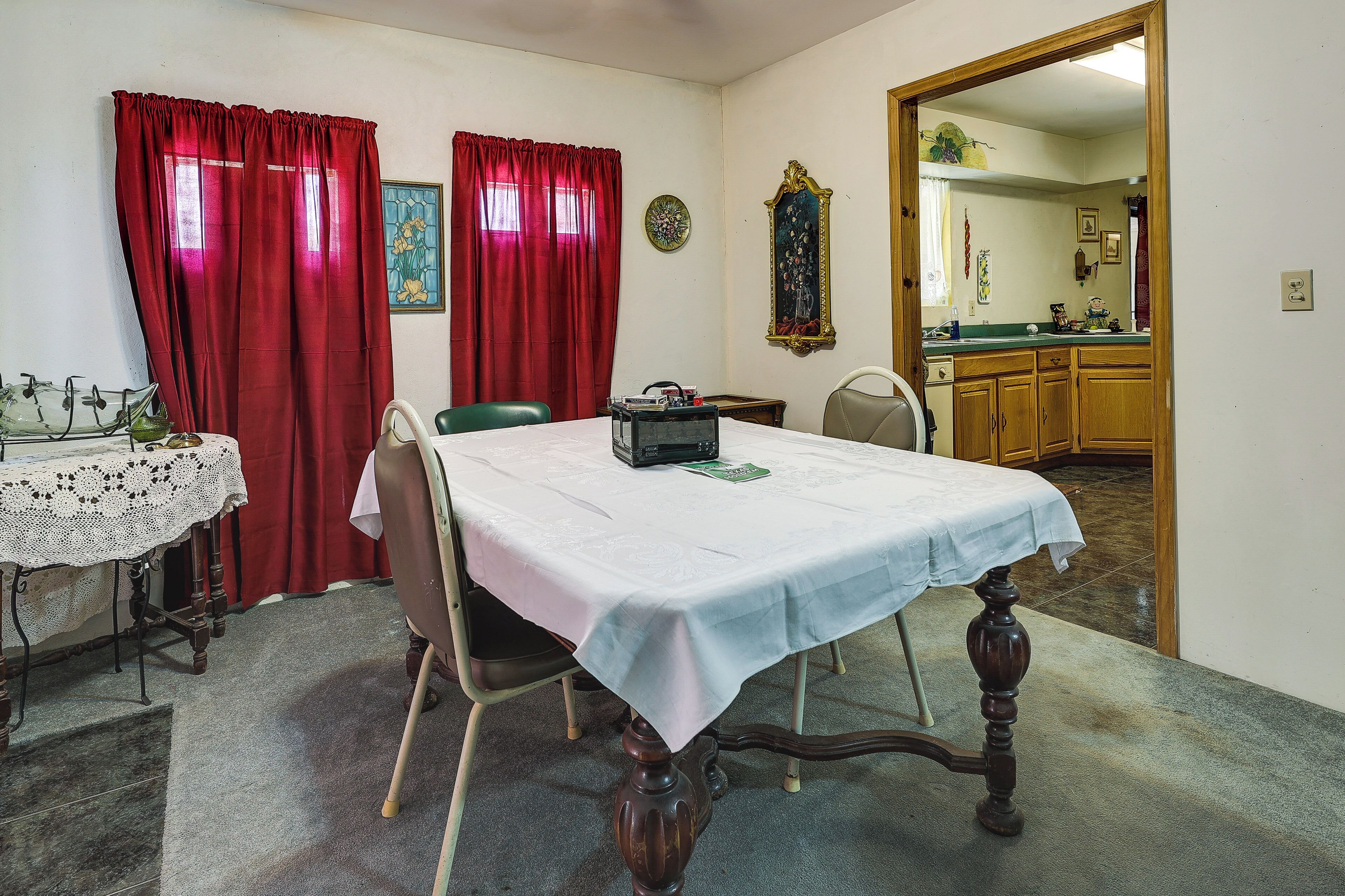 A dining area with a table set for four, a lace tablecloth, and a red curtain.