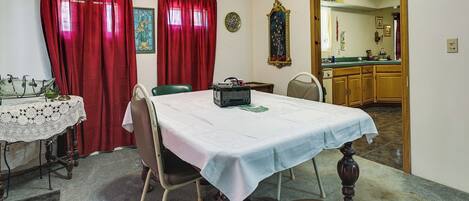 A dining area with a table set for four, a lace tablecloth, and a red curtain.