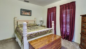 Quarto com cama de madeira, mesa de cabeceira com abajur, cômoda e janela com cortinas vermelhas.