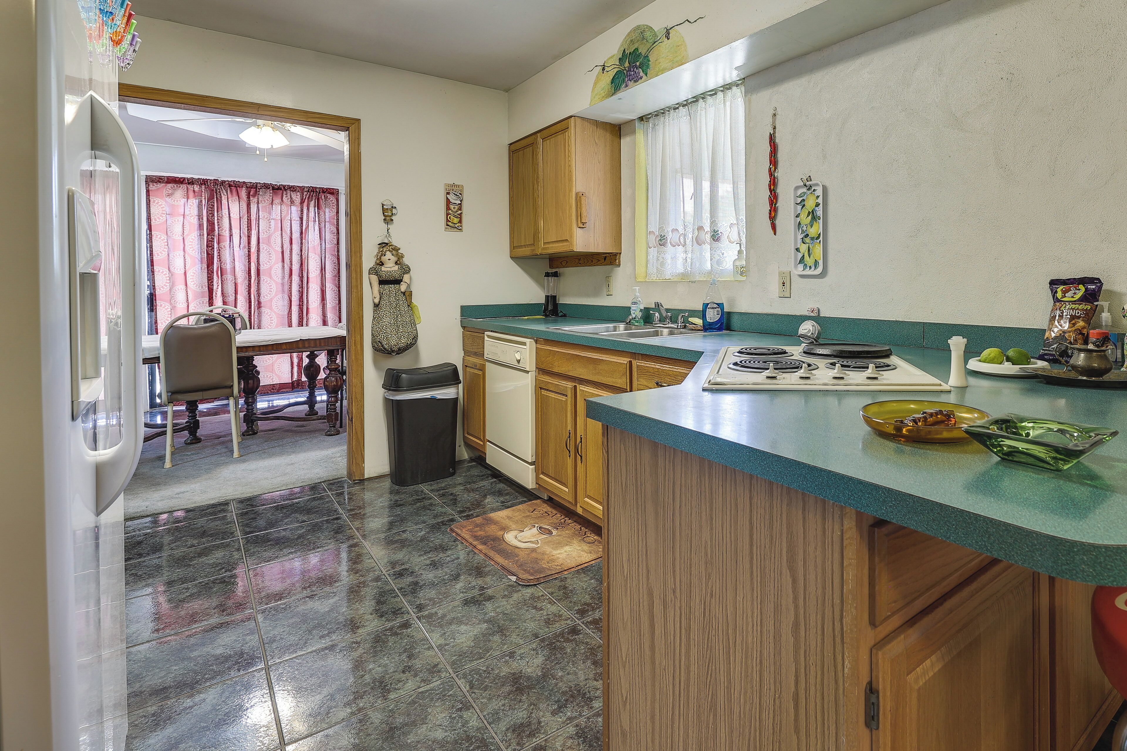 A kitchen with a stove, sink, and wooden cabinets. There is a dining area with a table and chairs visible through an open door.
