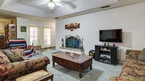 Uma sala de estar com uma grande mesa de centro de madeira, dois sofás estampados, uma televisão e uma peça decorativa na parede.
