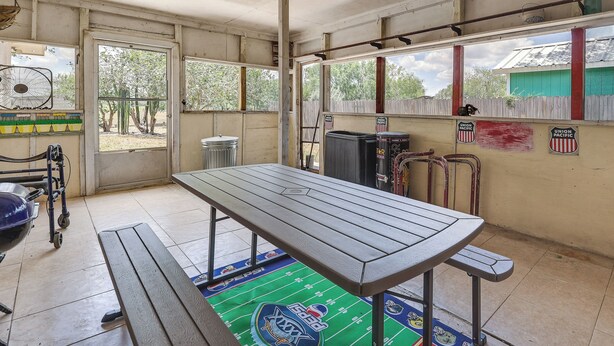 Um quarto com uma mesa grande, um ventilador, uma janela e uma porta.