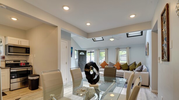 A modern kitchen with built-in appliances, a dining area with a glass table, and a living space with a sofa and cushions. - Stylish Harveys Lake Apt - Steps to the Water! (Harveys Lake)