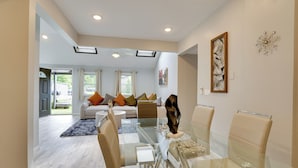 A modern living room with a glass dining table, beige sofas, and a large window. - Stylish Harveys Lake Apt - Steps to the Water! (Harveys Lake)