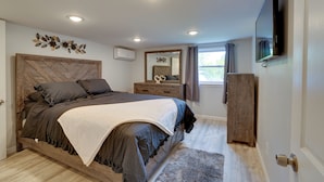 A bedroom with a wooden bed, a dresser, a TV mounted on the wall, and a window with curtains. - Stylish Harveys Lake Apt - Steps to the Water! (Harveys Lake)