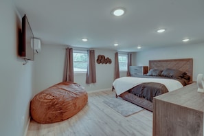 A modern bedroom with a large bed, a bean bag chair, a wooden headboard, a TV, and a window with curtains. - Stylish Harveys Lake Apt - Steps to the Water! (Harveys Lake)
