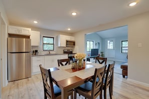 A modern kitchen with white cabinets, a stainless steel refrigerator, and a dining area with a wooden table and chairs. - Second-floor Harveys Lake Apartment With Deck! (Harveys Lake)