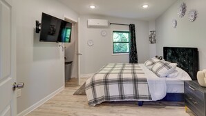 Un dormitorio con cama, televisor montado en la pared, aire acondicionado y decoración en las paredes.