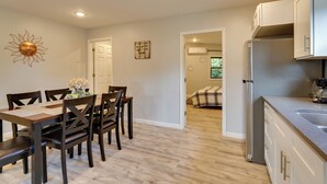 Una cocina moderna con un refrigerador de acero inoxidable, una mesa de comedor de madera con sillas y un pasillo que conduce a un dormitorio.