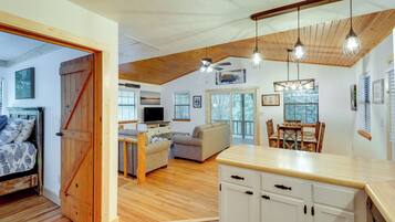 A spacious living area with a wooden ceiling, a dining table with chairs, a sofa, and a kitchen area with white cabinets.