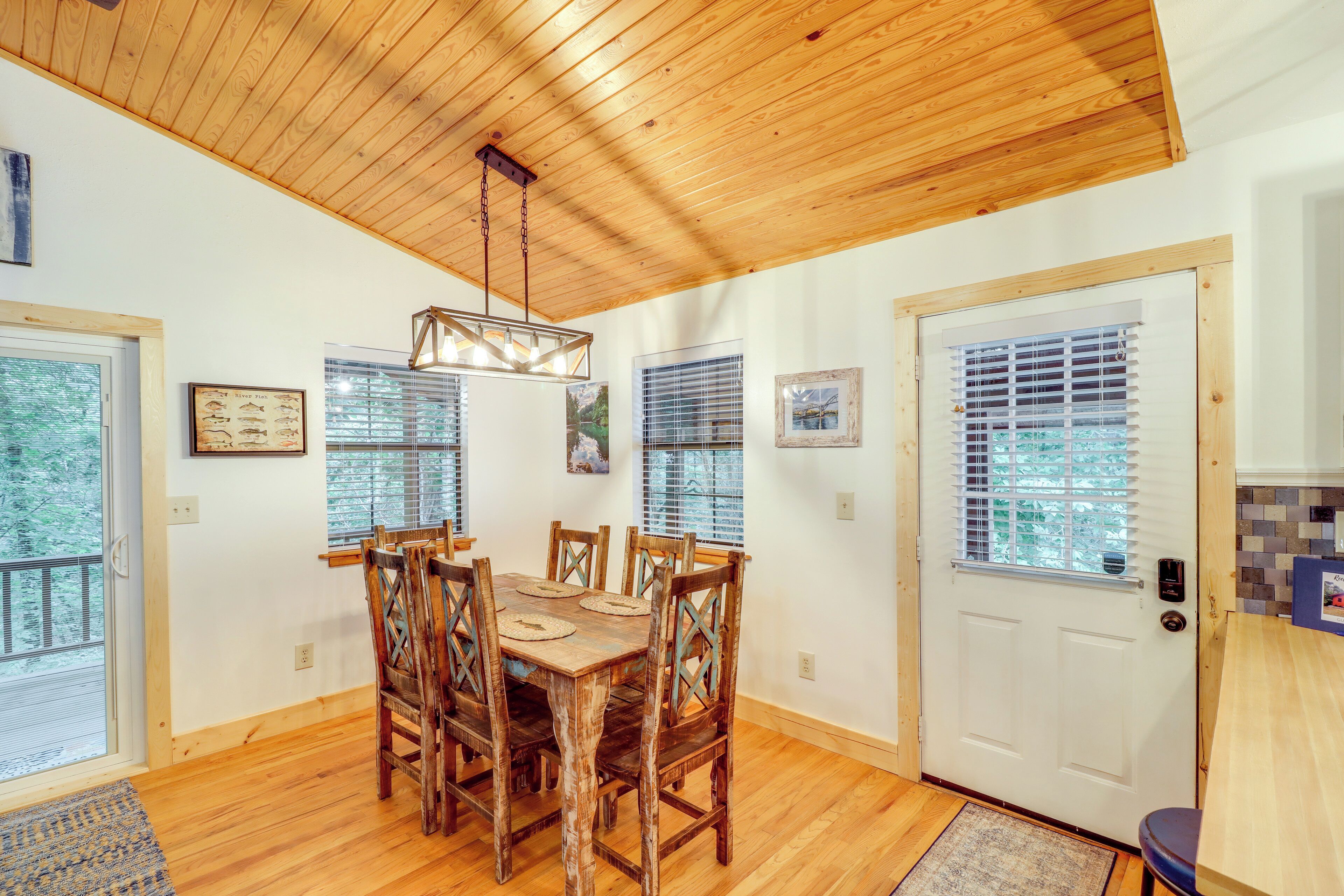 A dining area with a wooden table and chairs, wooden ceiling, and windows with blinds.