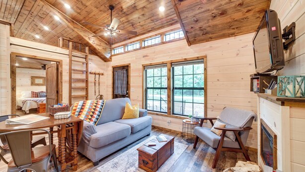 A cozy cabin interior with a wooden ceiling, a sofa, a dining table, and a fireplace. - Mcalester Vacation Rental w/ Private Hot Tub (McAlester)