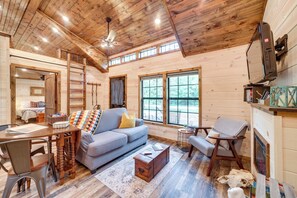 A cozy cabin interior with a wooden ceiling, a sofa, a dining table, and a fireplace. - Mcalester Vacation Rental w/ Private Hot Tub (McAlester)