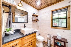 A wooden cabin bathroom with a sink, toilet, and window. - Mcalester Vacation Rental w/ Private Hot Tub (McAlester)