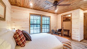 A wooden cabin bedroom with a bed, pillows, a desk, and a chair. - Mcalester Vacation Rental w/ Private Hot Tub (McAlester)