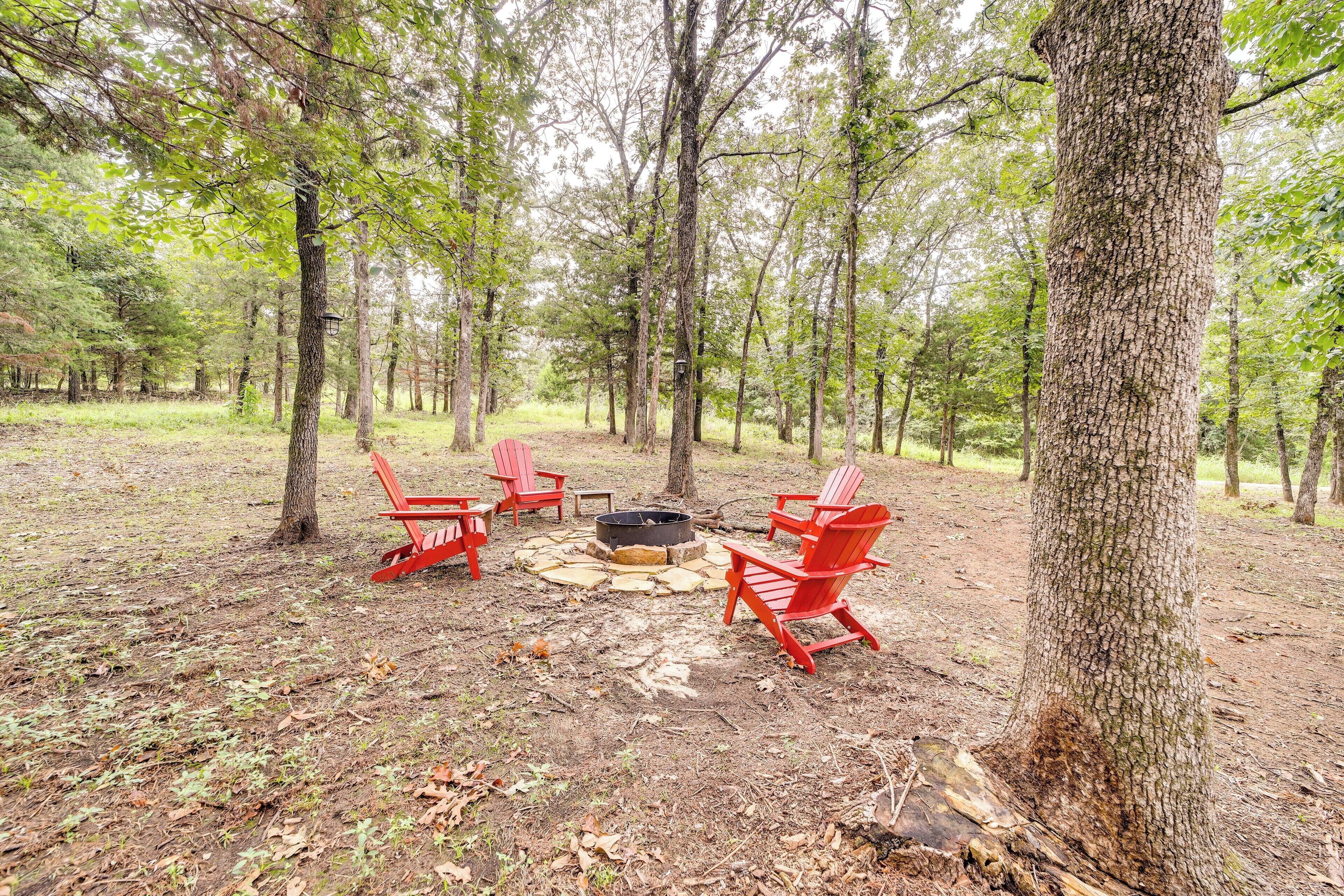 A forest campsite with red chairs and a fire pit.