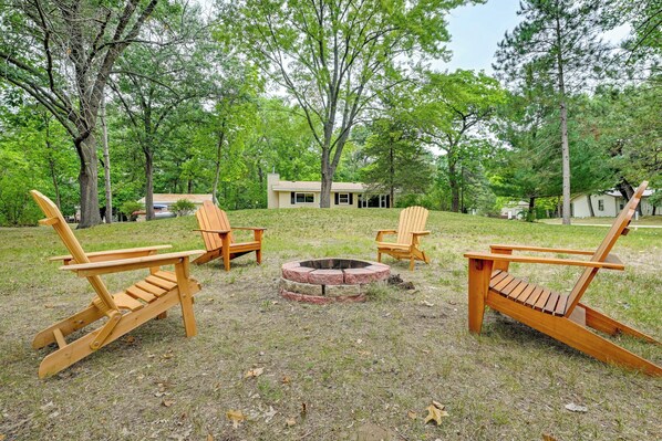 Un patio trasero con tres sillas Adirondack dispuestas alrededor de un brasero circular.