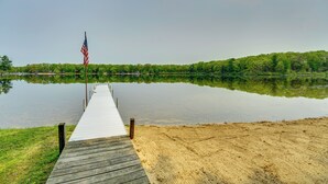 A wooden pier extending into a calm lake with a sandy beach on one side and a forested area in the background. - Long Lake Cabin w/ Kayaks, Private Beach & Dock! (Fountain)