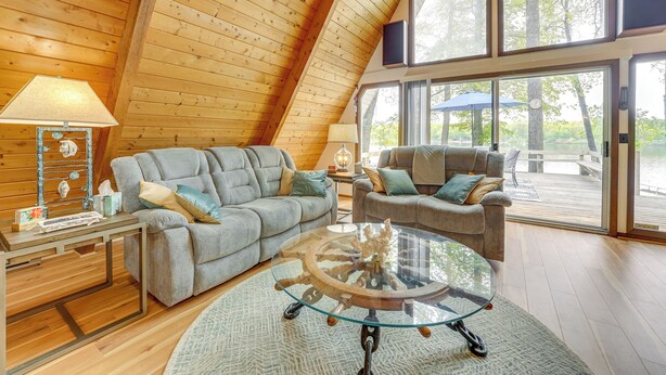 A cozy living room with a high ceiling, wooden walls, and large windows offering a view of the outdoors. - Long Lake Cabin w/ Kayaks, Private Beach & Dock! (Fountain)