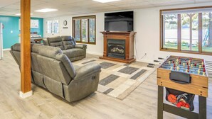 A living room with a fireplace, a foosball table, and a large window offering a view of a park. - Lakefront Arkansas Escape w/ Grill, Dock & Kayaks! (Horseshoe Bend)
