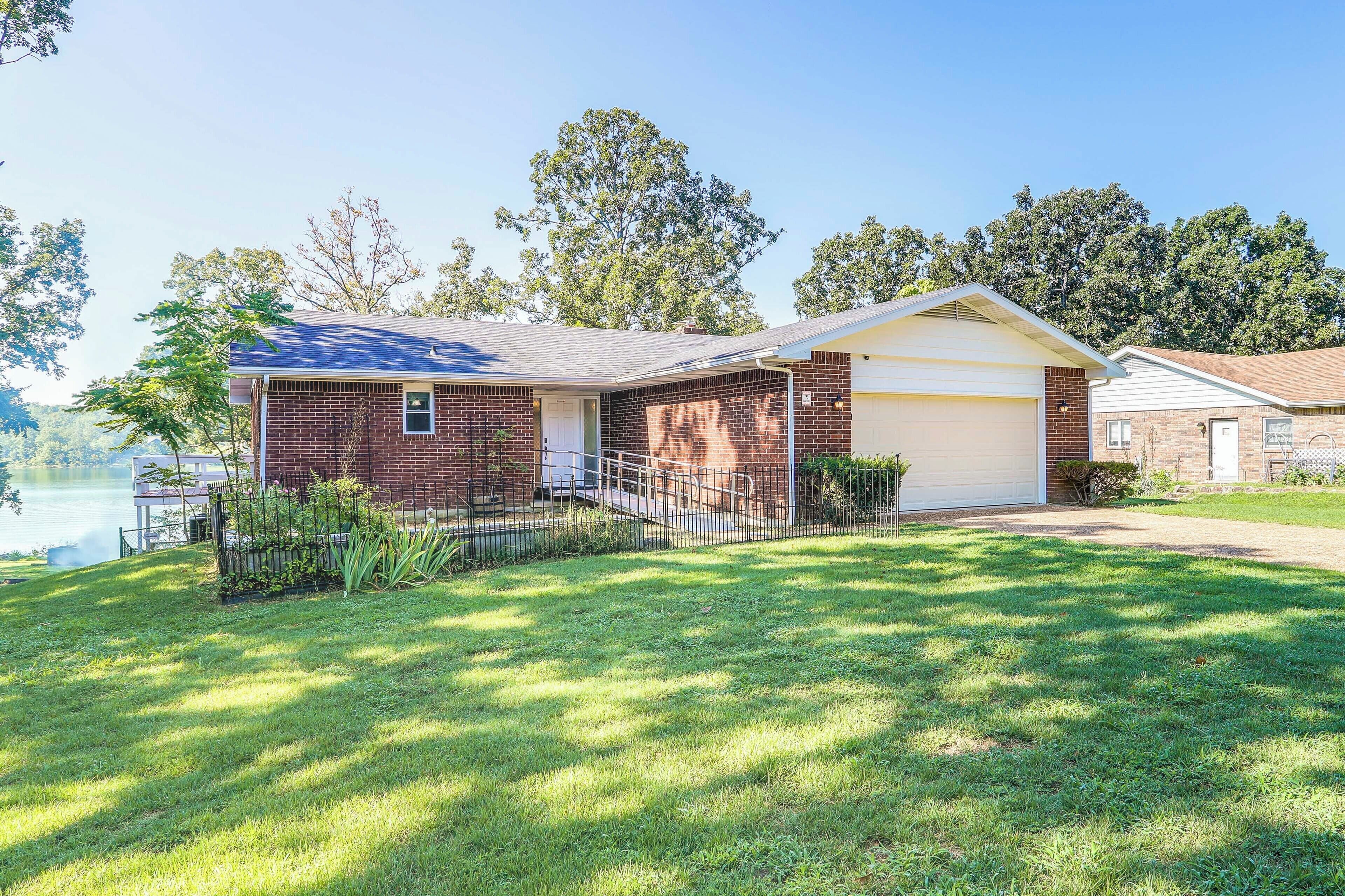 A single-story brick house with a garage, a fenced yard, and a lake view.