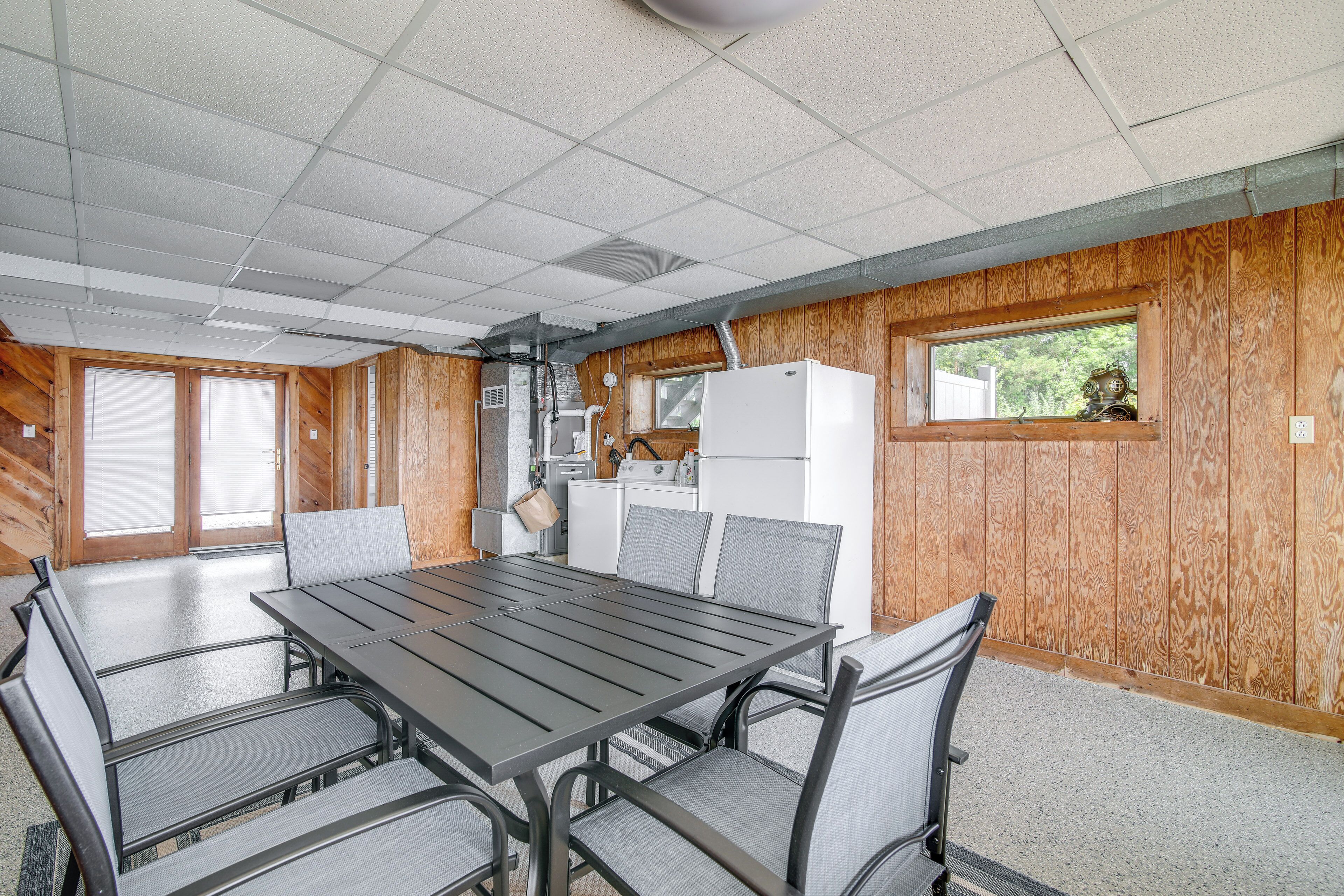 A dining area with a long table and chairs, wooden walls, and a window with a view.