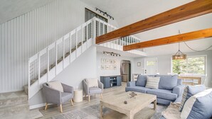 Un salon spacieux avec un escalier, un ensemble de canapés bleus, une table basse en bois et une grande fenêtre qui laisse entrer la lumière naturelle.