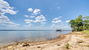 A beach with clear water, a pier, and trees. - Fishermans Paradise: Lake-view Home in Many! (Many)