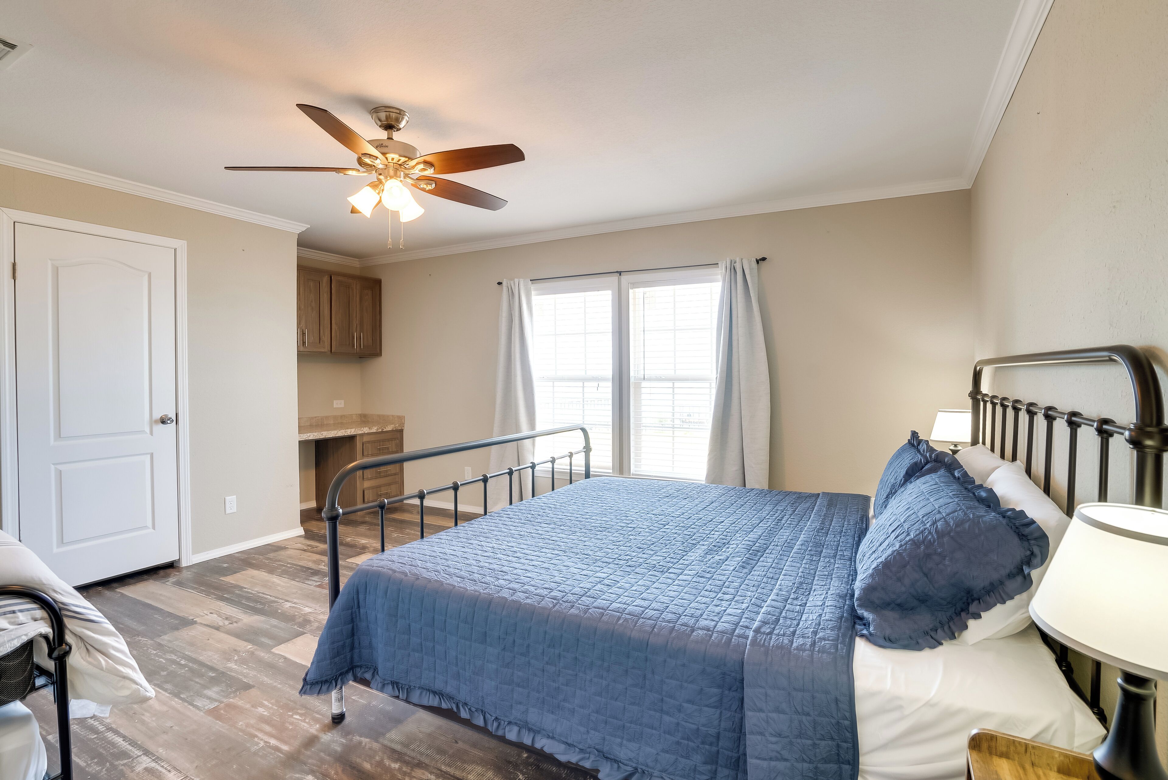 A bedroom with a bed, a ceiling fan, a window with curtains, and a door.