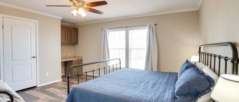 A bedroom with a bed, a ceiling fan, a window with curtains, and a door.