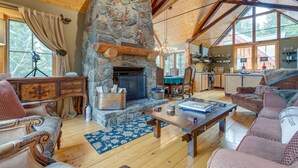 Un intérieur de chalet chaleureux avec une cheminée en pierre, des meubles en bois et de grandes fenêtres.