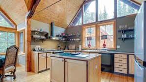 Une cuisine spacieuse dotée de meubles en bois, d’un îlot central et de grandes fenêtres offrant une vue sur l’extérieur.