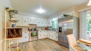 A modern kitchen with white cabinets, stainless steel appliances, and a glass dining table. - Charming Jonesville Home w/ Grill - Near Wineries! (Jonesville)