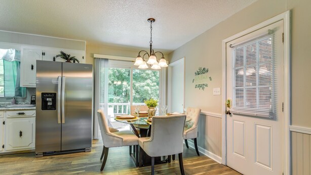A modern kitchen with a stainless steel refrigerator, a dining table with chairs, and a window with blinds. - Charming Jonesville Home w/ Grill - Near Wineries! (Jonesville)
