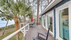 Una terraza de madera con una mesa y sillas, con vista a una playa y palmeras.