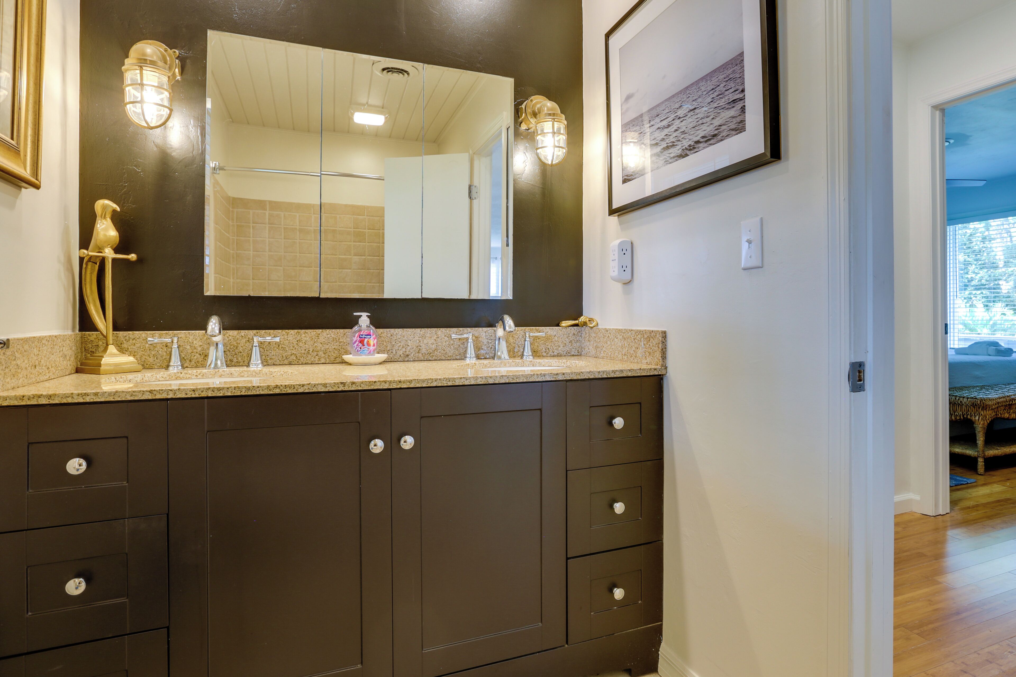 A bathroom with dark brown cabinets, a large mirror, and a countertop with a soap dispenser.