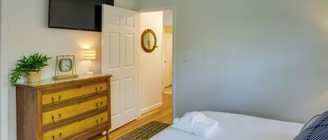 A bedroom with a bed, a dresser, a TV mounted on the wall, and a door leading to another room.