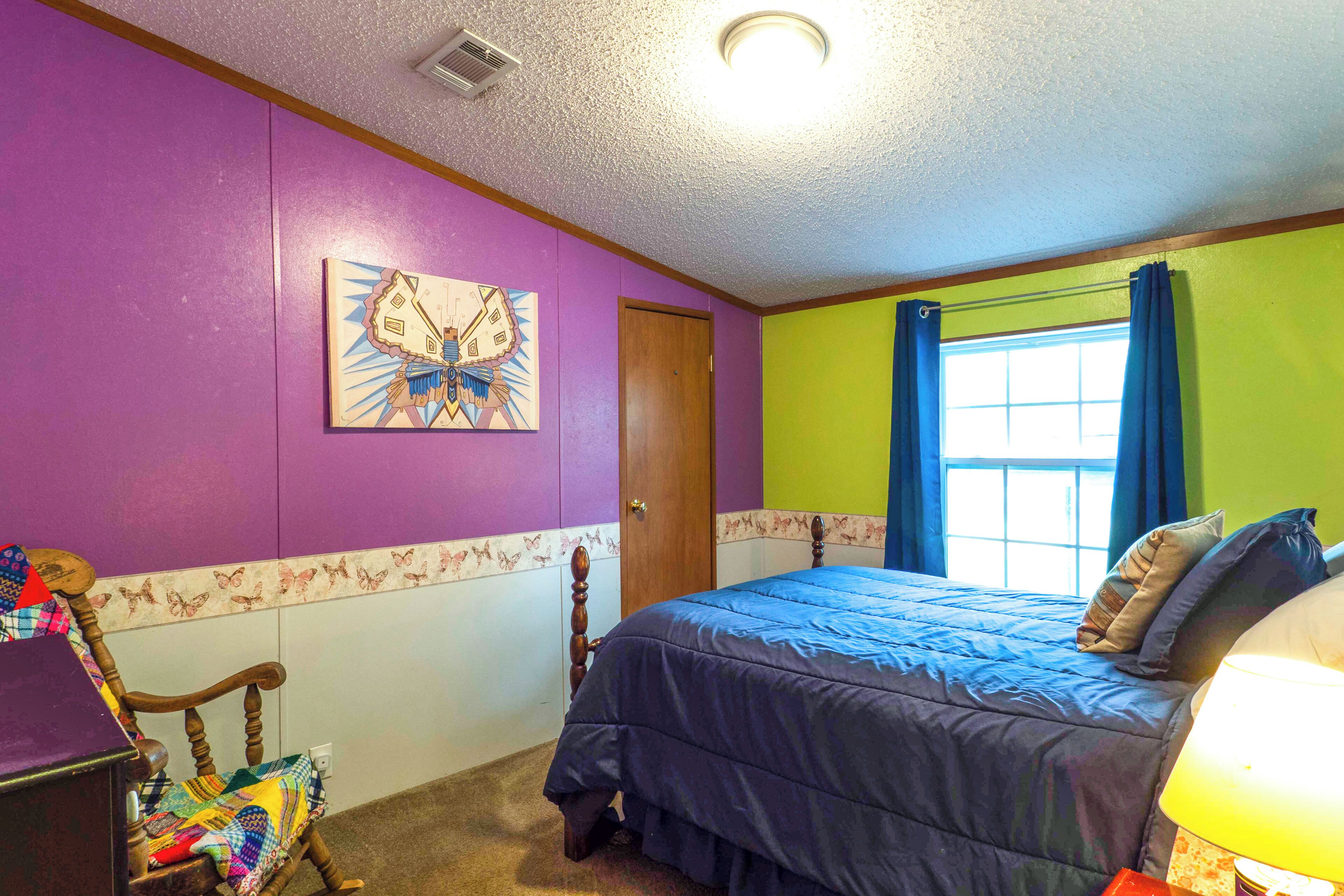 Un dormitorio con cama, una silla, una puerta y una ventana con cortinas.