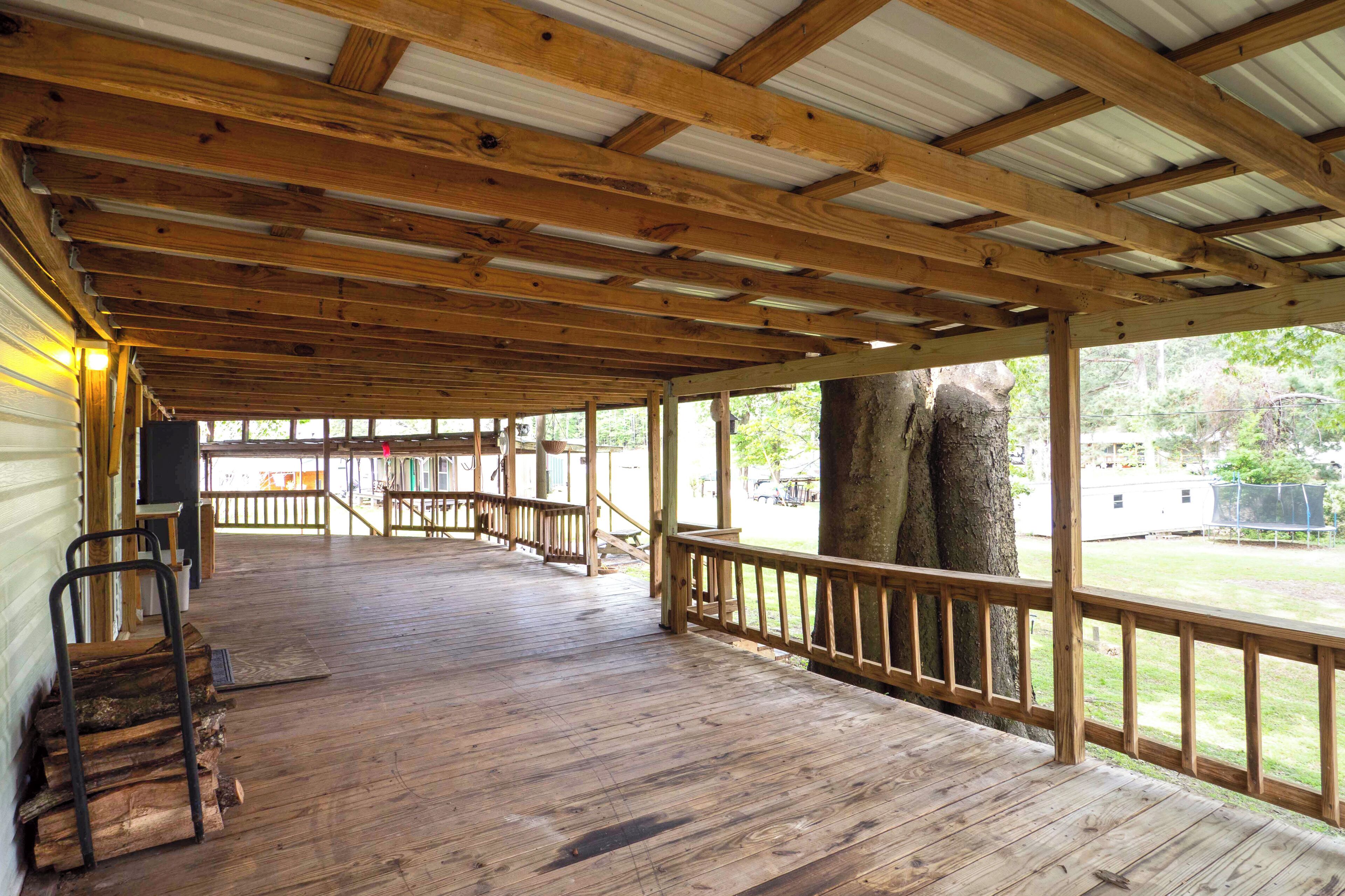 A covered wooden deck with a railing, wooden steps, and a view of the outdoors.