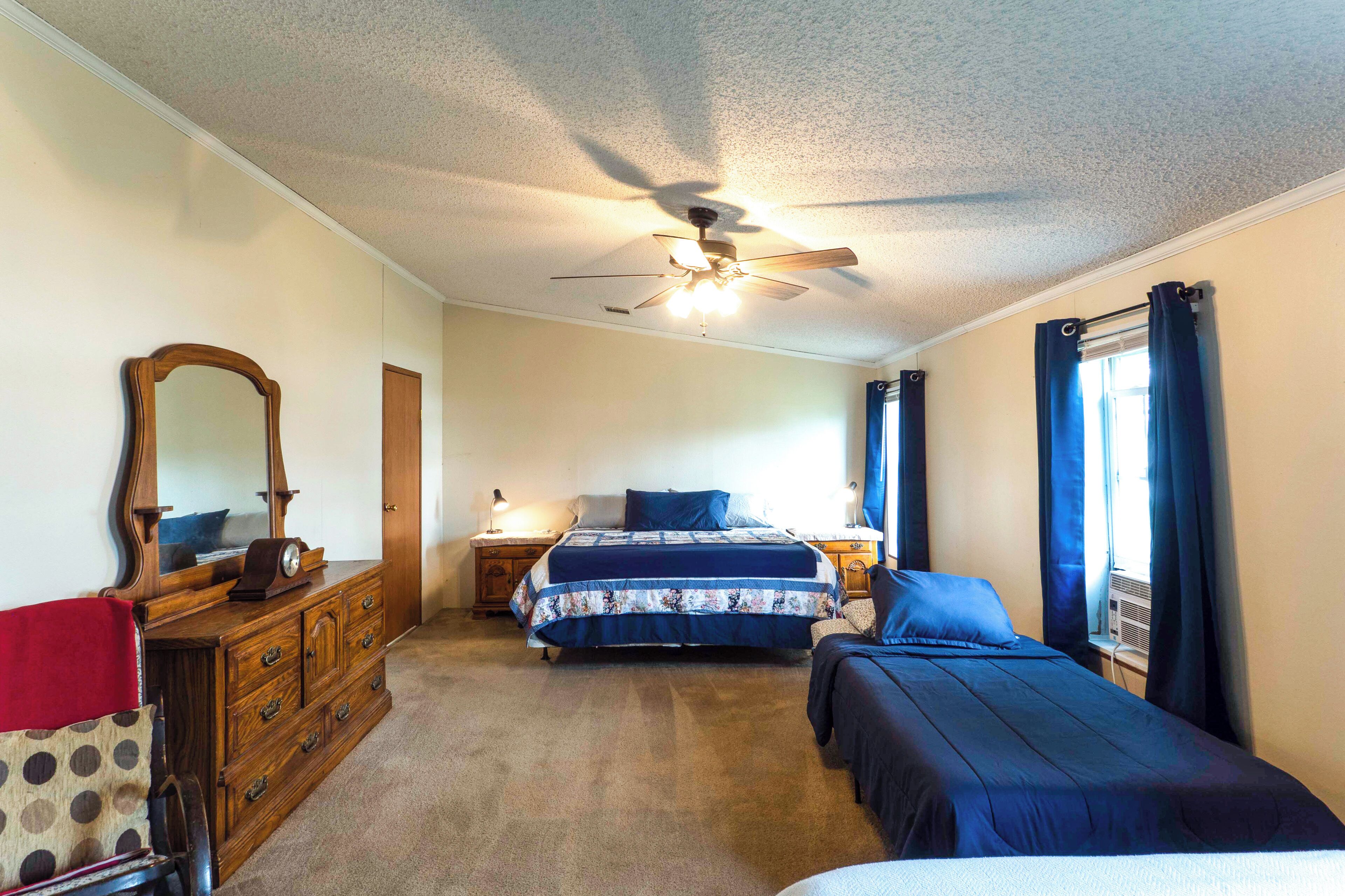 Quarto com duas camas, um ventilador de teto, cômoda e janela com cortinas.