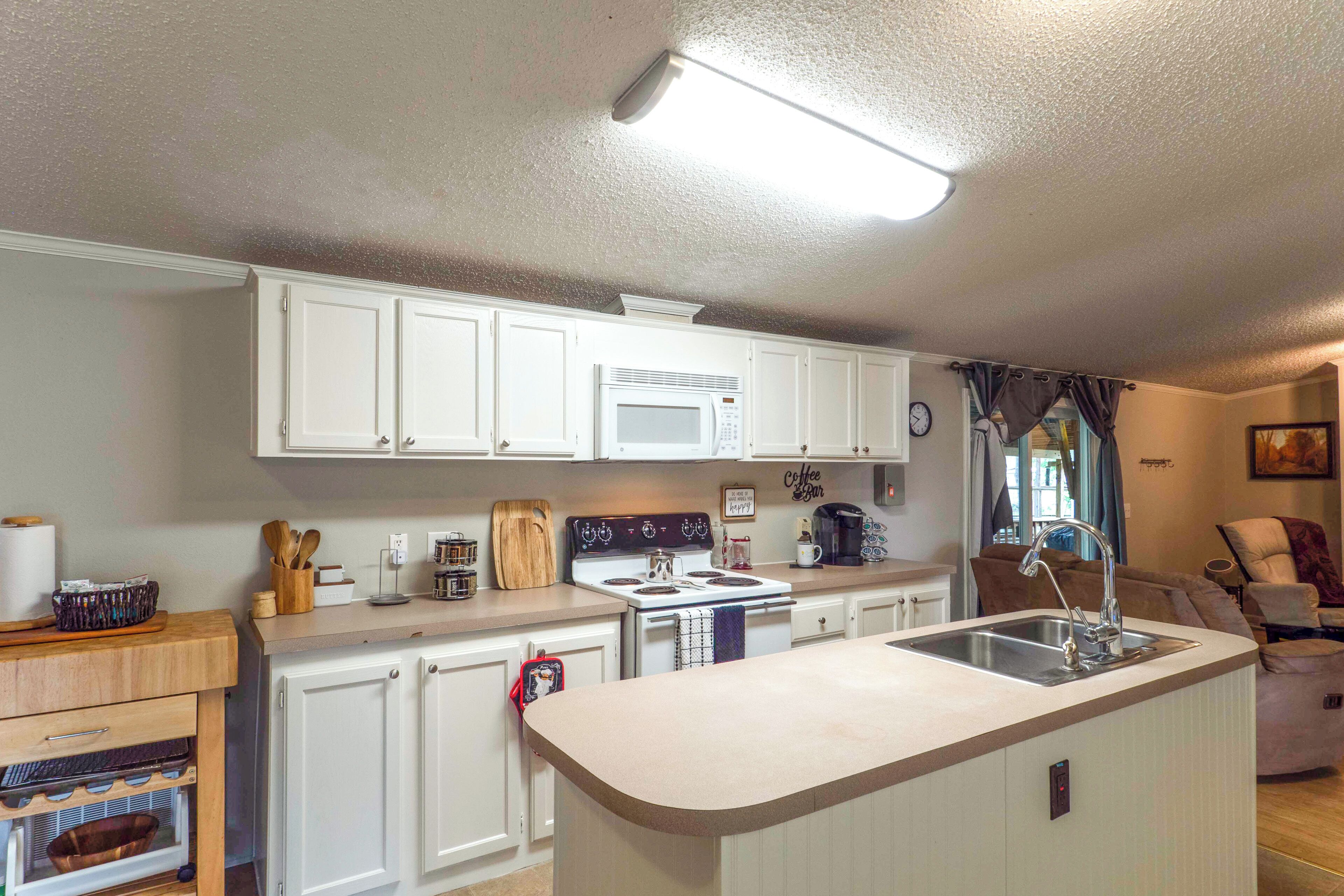 A kitchen with white cabinets, a microwave, a stove, and a sink.